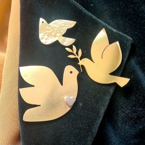 A coat lapel showing 3 brass pins in the shape of doves